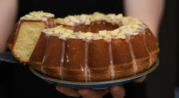 Wilgotna babka wielkanocna, ozdobiona lukrem i płatkami migdałów, prezentuje się apetycznie. Kawałek ciasta został już odcięty.