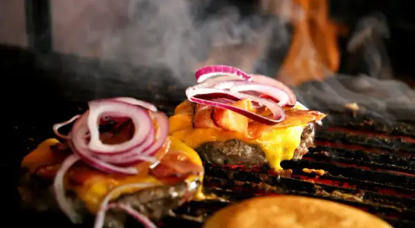 Pyszne burgery z grilla z roztopionym serem i czerwoną cebulą, parujące na ruszcie.