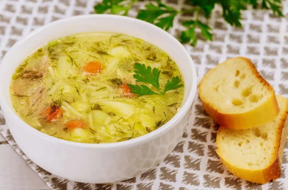 Aromaticzna zupa wiosenna z kawałkami kurczaka, ziemniaków i marchewki, posypana świeżym koperkiem. Obok kromki chleba.