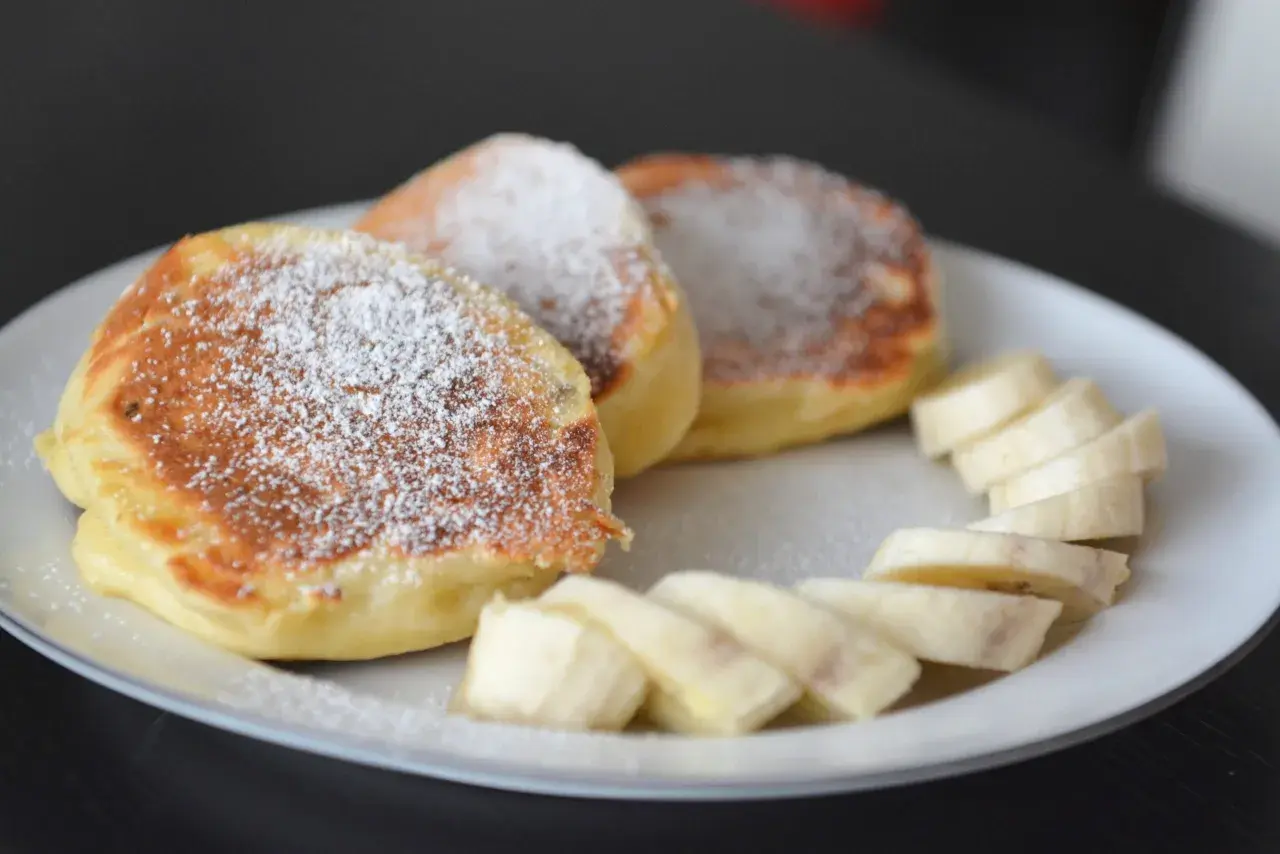 Puszyste, szybkie placuszki na śniadanie posypane cukrem pudrem, obok plasterki banana. Idealne na dobry początek dnia.