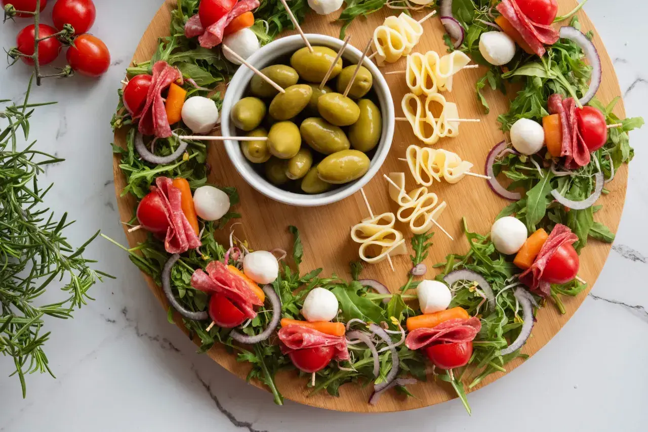 Idealne przekąski na ognisko: szaszłyki z pomidorkami, mozzarellą, salami i marchewką, a obok miseczka oliwek i serowe zawijasy.