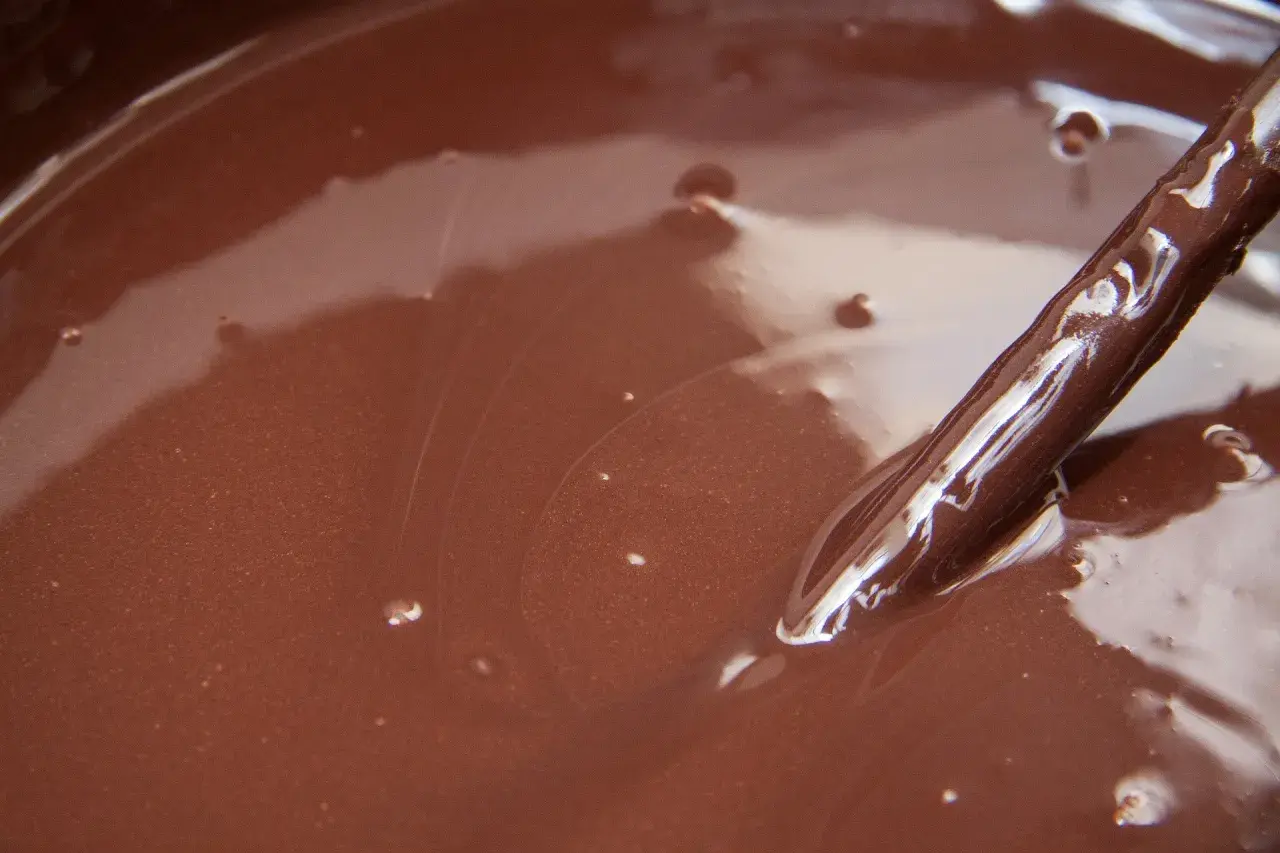 Gładki, błyszczący ganache czekoladowy w misce, z widoczną drewnianą łyżką zanurzoną w jego aksamitnej masie.