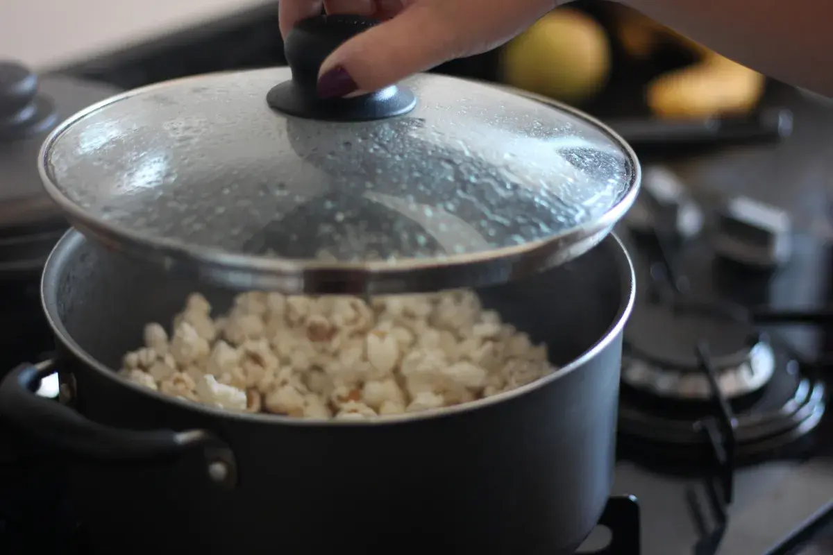 Ręka podnosi pokrywkę garnka, odsłaniając pyszny, świeżo zrobiony popcorn. Idealny sposób, jak zrobić popcorn na wieczór filmowy.