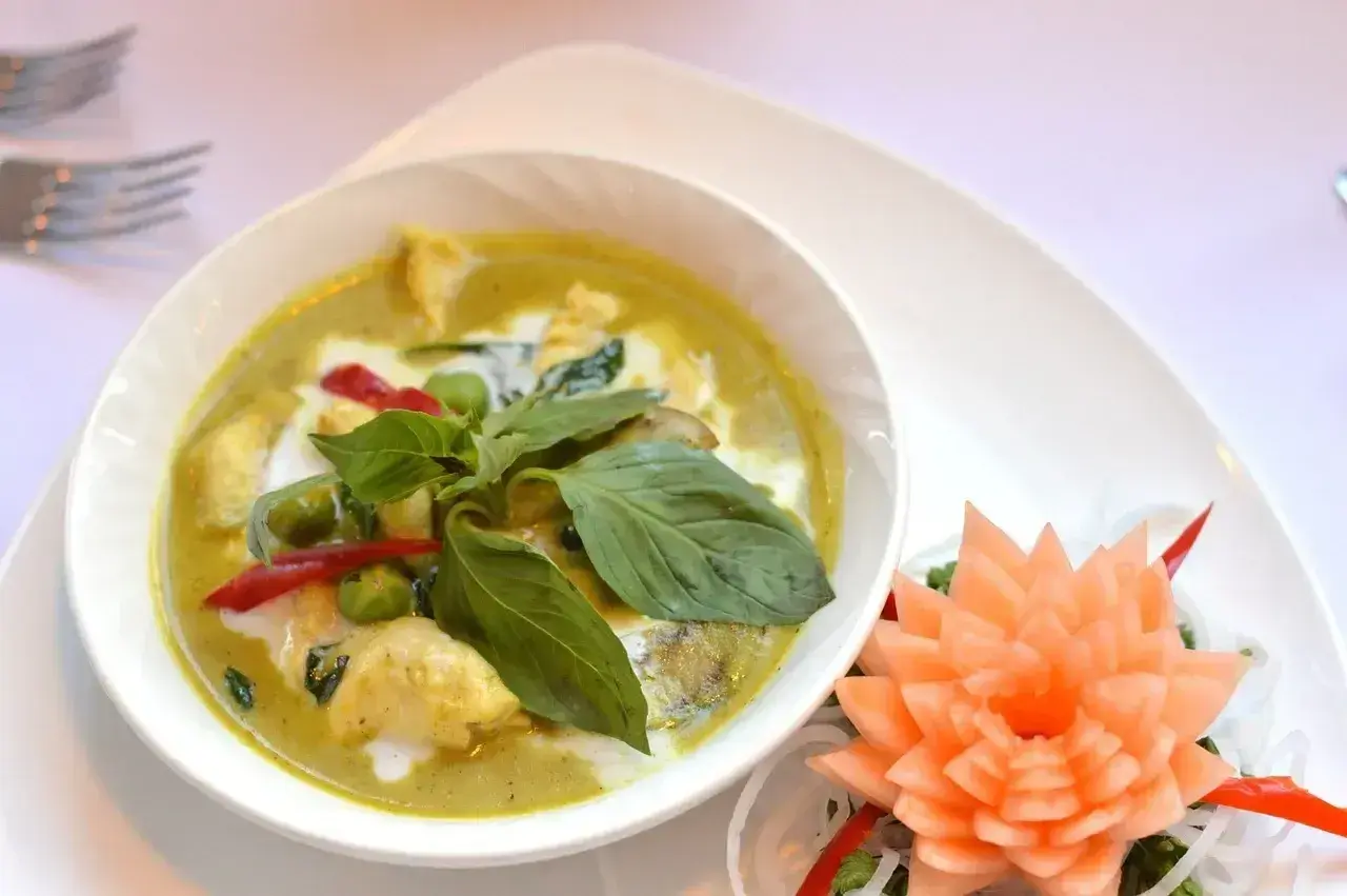 Zielony curry z kurczakiem, podany z bazylią i papryczką chili. Obok ozdobna rzeźba z marchewki.