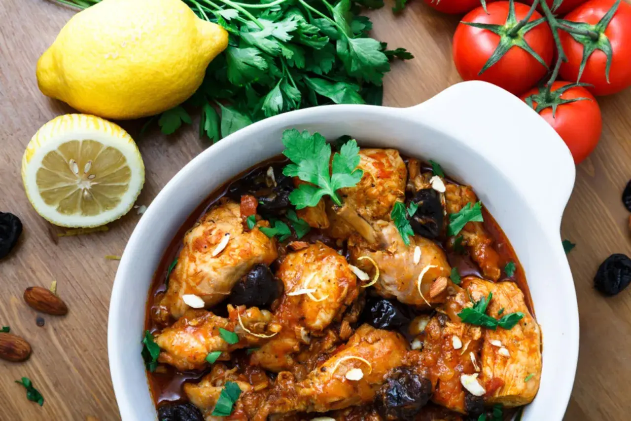 Aromatyczny tagine z kurczakiem, śliwkami i migdałami, podany z cytryną i pomidorami.
