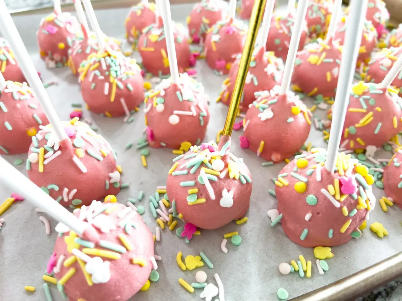 Różowe cake pops z kolorową posypką i króliczkami, idealne na wielkanocny przepis.