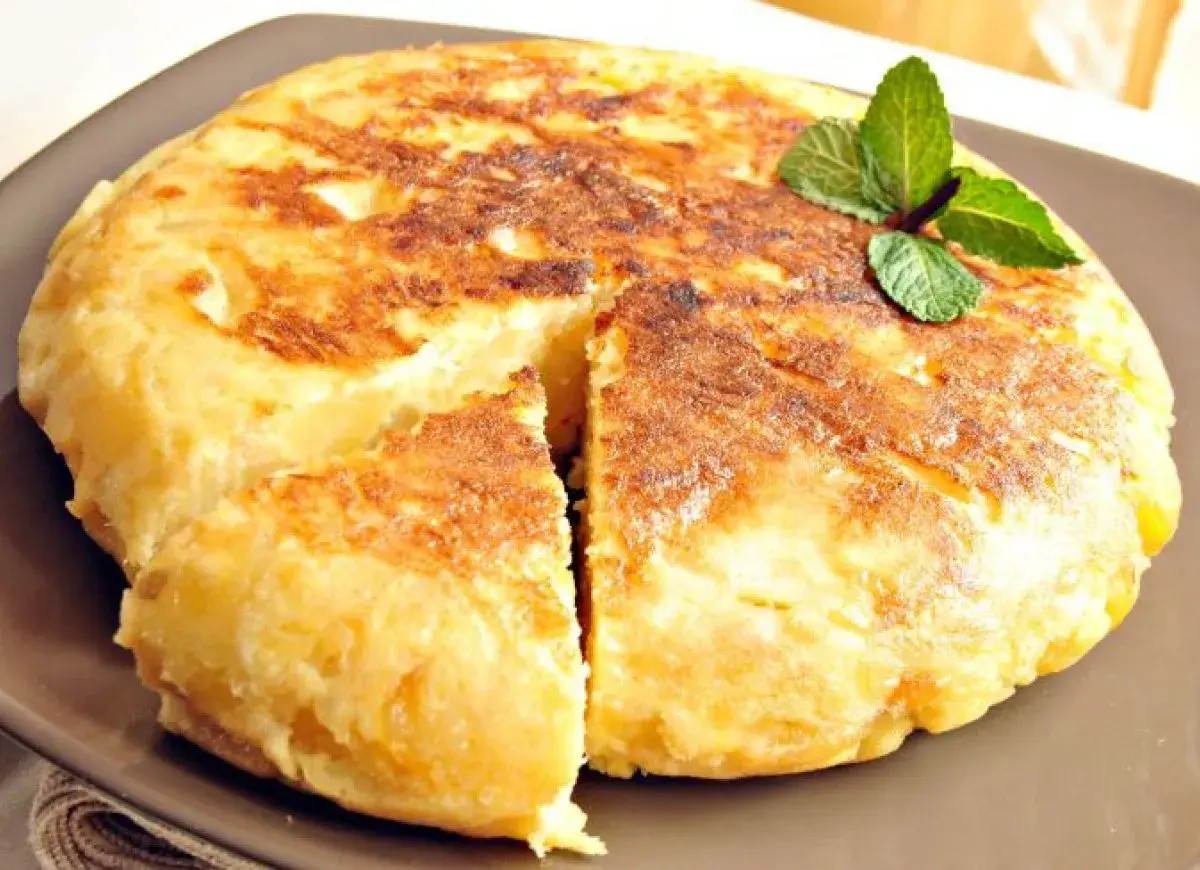 Pyszna tortilla de patatas, złocista i puszysta, z gałązką mięty na wierzchu.