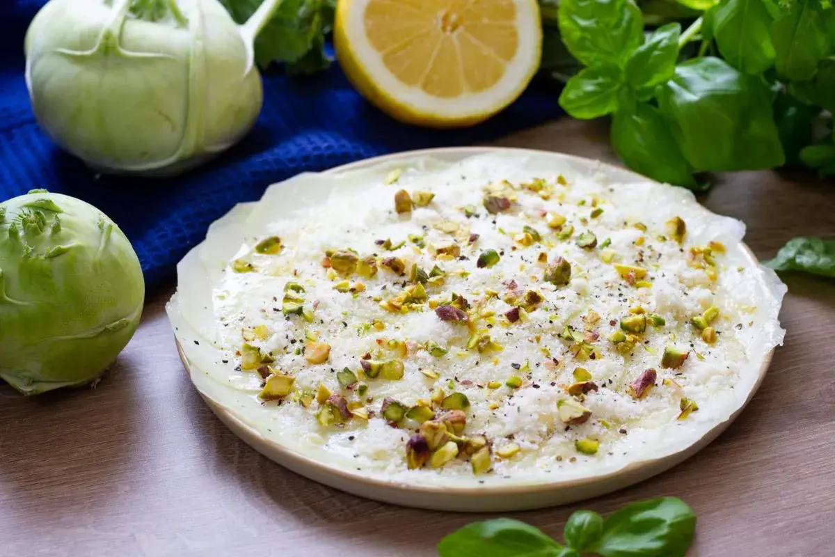 Delikatne carpaccio z kalarepy, posypane pistacjami i parmezanem, z dodatkiem świeżej bazylii i cytryny.
