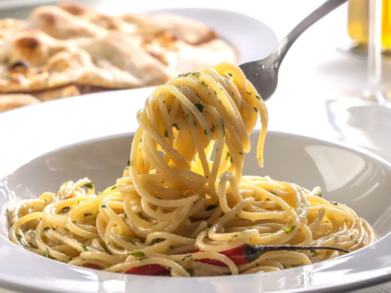 Pyszny, aromatyczny makaron spaghetti z czosnkiem i chili, idealny przepis na szybki makaron. Na talerzu widać też pieczywo.