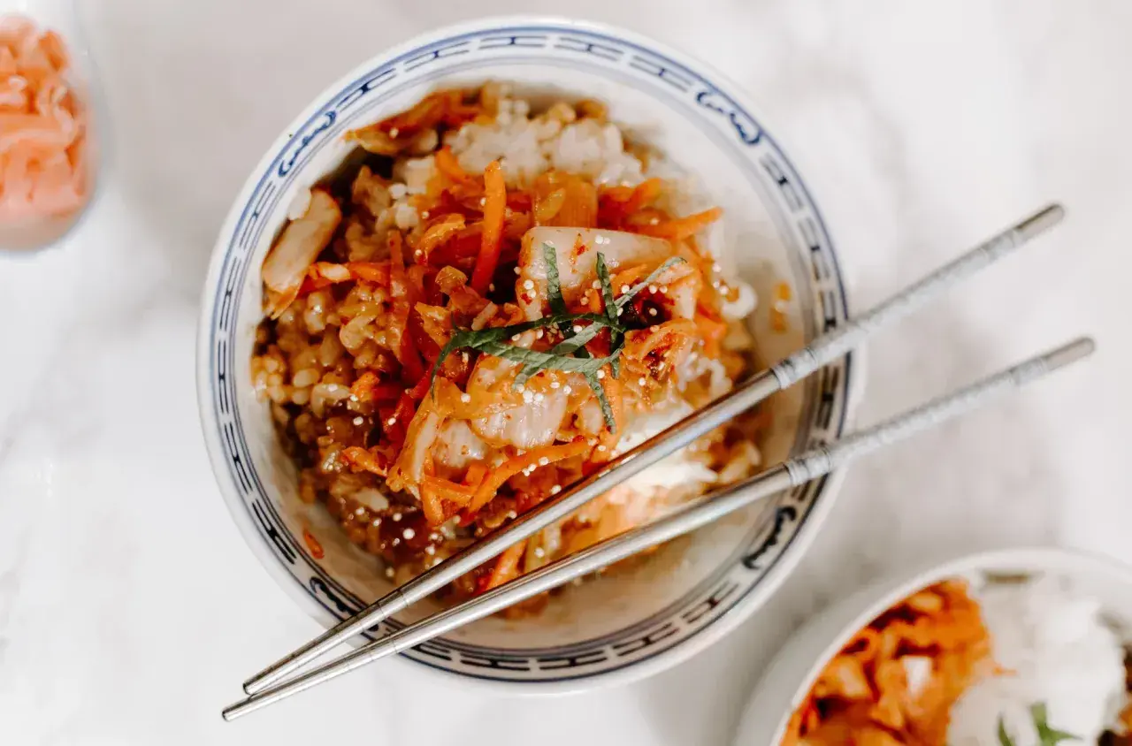 Miseczka ryżu z pikantnym kimchi i marchewką, pałeczki gotowe do jedzenia. Kimchi co to? To fermentowana kapusta.