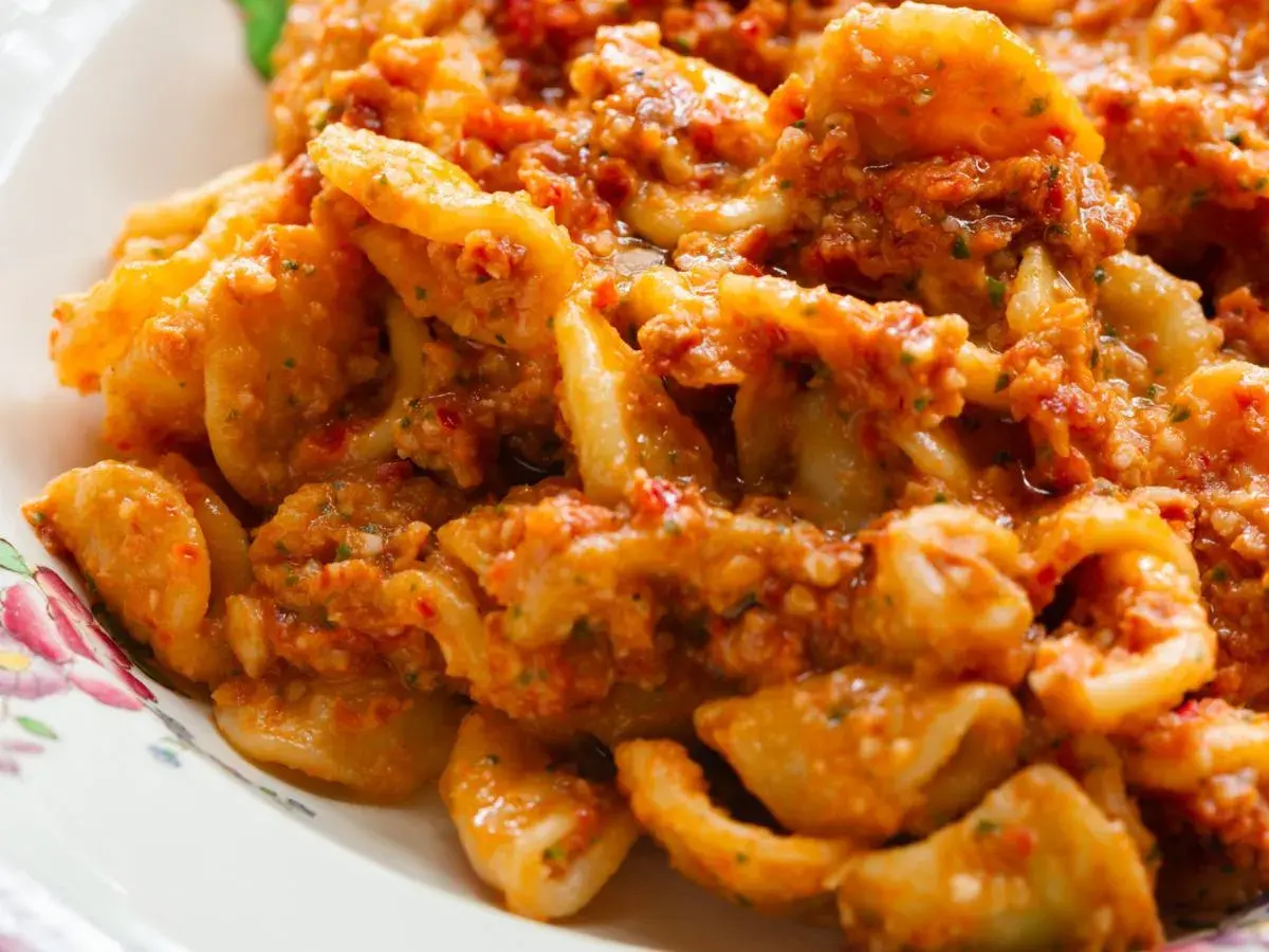 Pyszny makaron z pesto, pełen aromatycznych ziół i pomidorów, podany na talerzu z delikatnym wzorem.