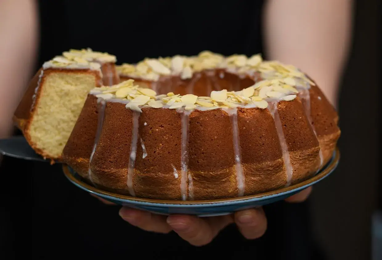 Wilgotna babka wielkanocna, ozdobiona lukrem i płatkami migdałów, prezentuje się apetycznie. Kawałek ciasta został już odcięty.