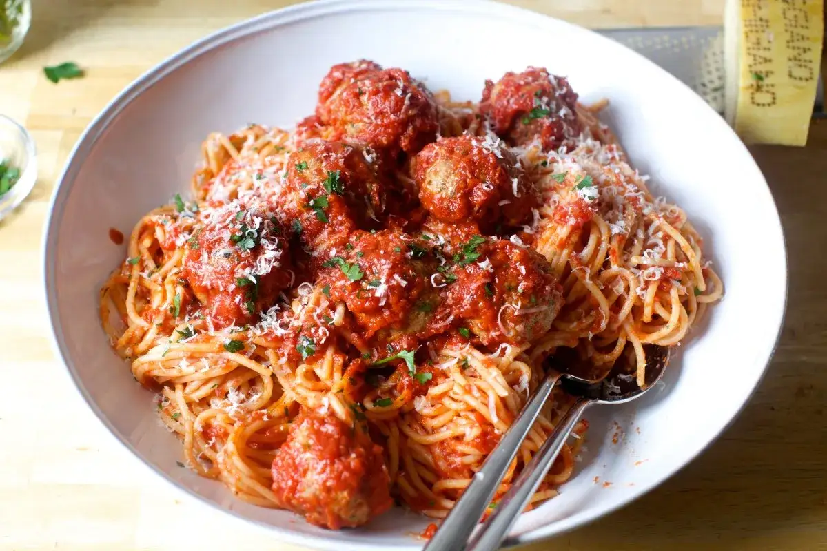 Szybki obiad dla dzieci i dorosłych: spaghetti z klopsikami w sosie pomidorowym, posypane parmezanem i natką pietruszki.