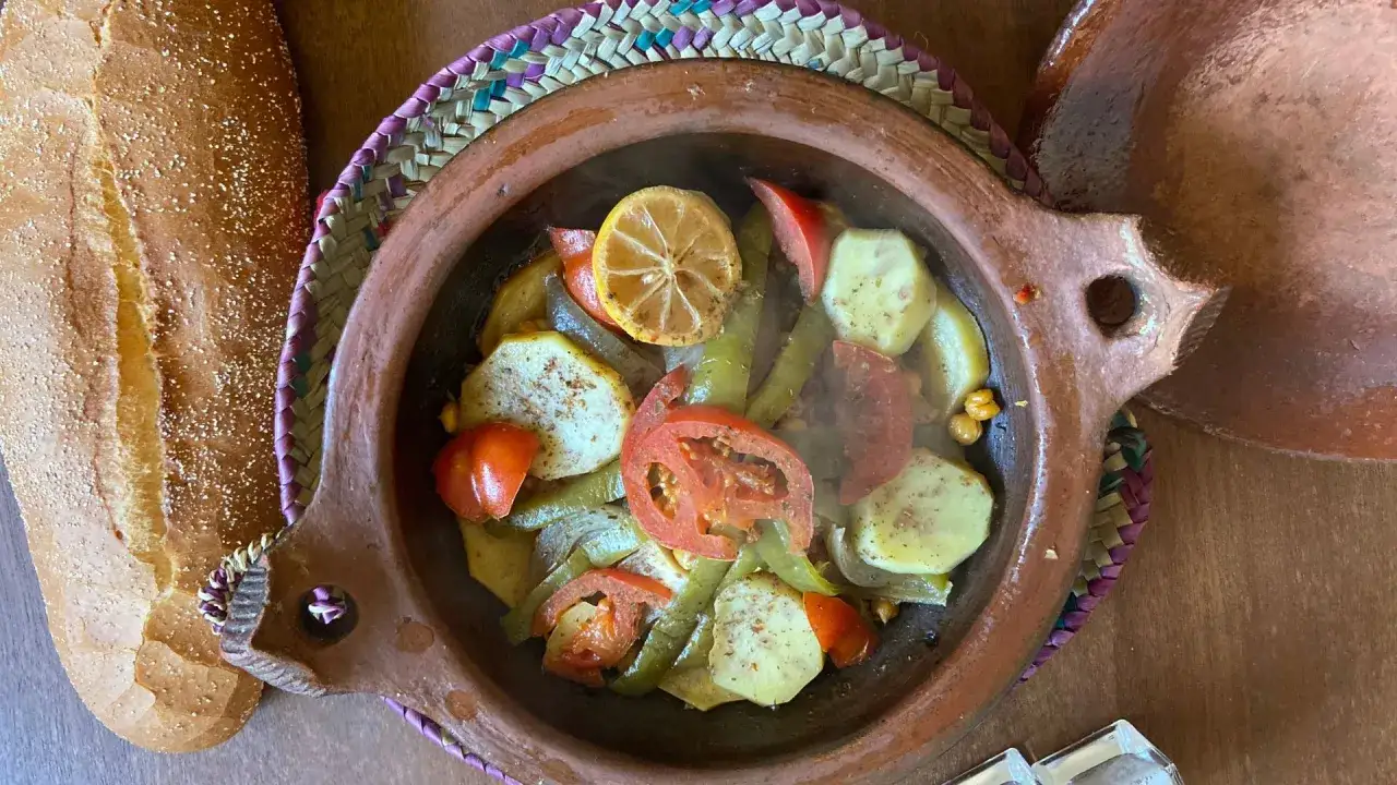 Aromatyczny tagine z kurczakiem, ziemniakami, pomidorami i cytryną, parujący w glinianym naczyniu, obok świeżego chleba.