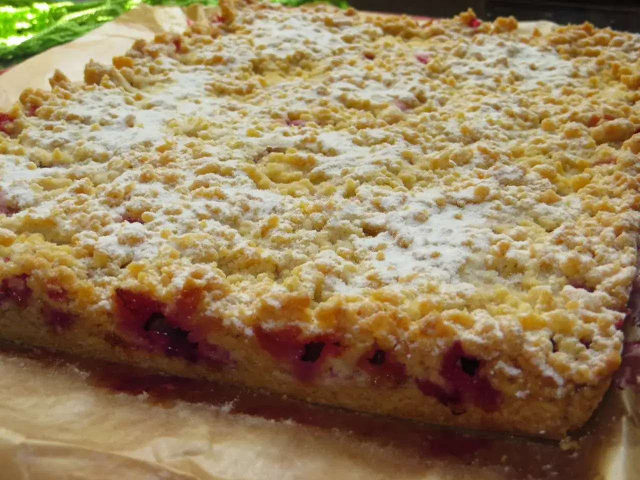 Pyszne ciasto ze śliwkami, posypane cukrem pudrem, z chrupiącą kruszonką i soczystymi owocami.