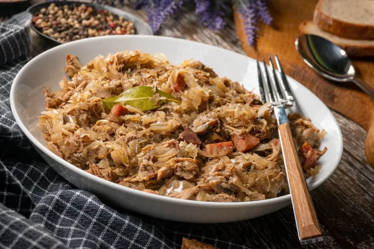 Pyszny bigos w białej misce, z widelcem. Zastanawiasz się, ile może stać bigos w lodówce? Nawet kilka dni, a smakuje coraz lepiej!