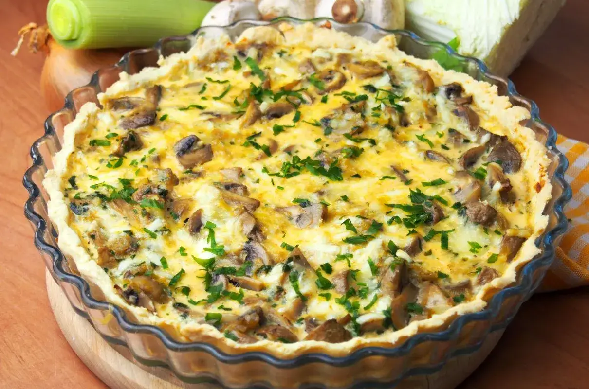 Pyszna tarta z porem i pieczarkami, posypana świeżą natką pietruszki, w szklanej formie.