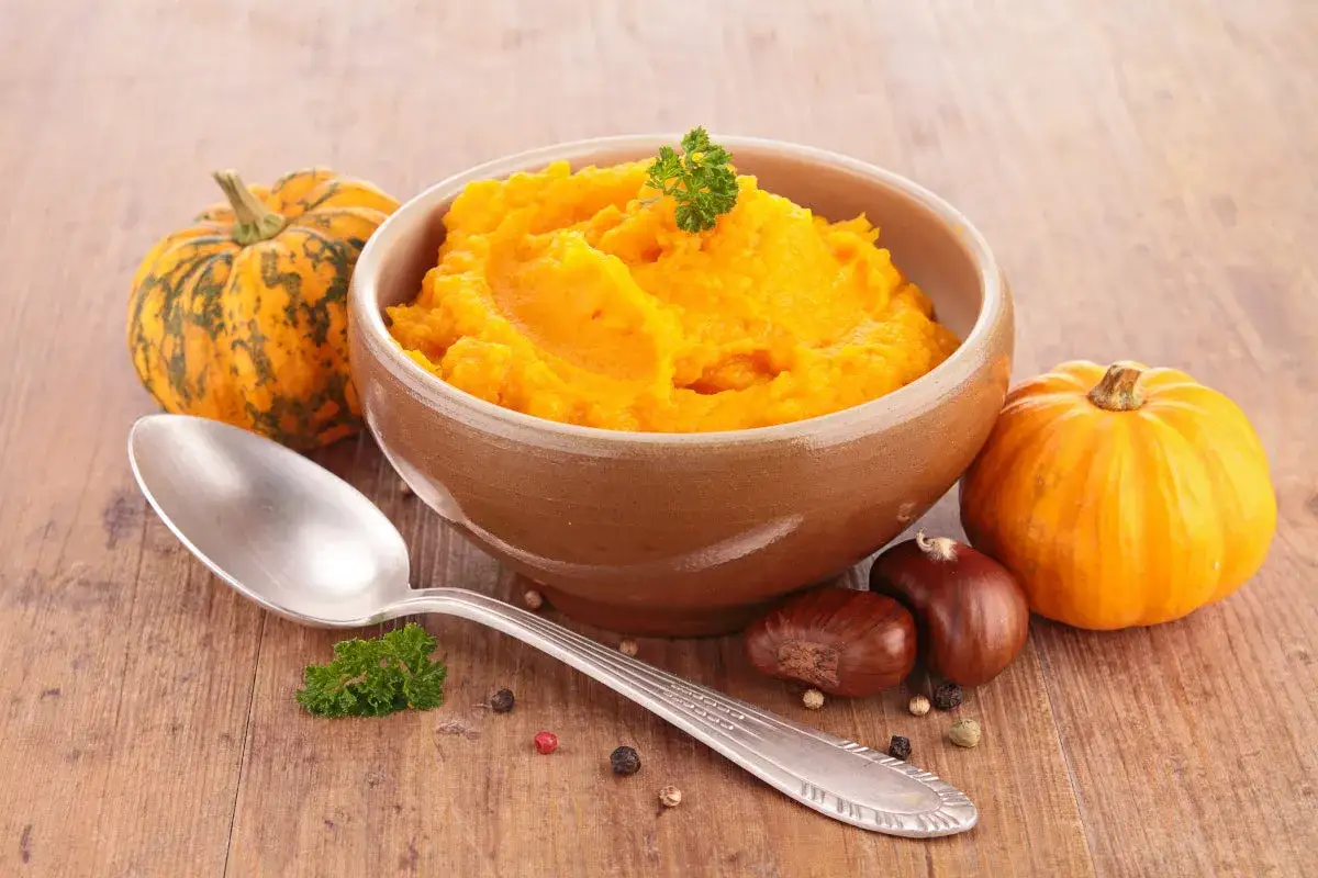 Aksamitne puree z dyni w glinianej misce, obok małe dynie, kasztany i łyżka. Idealne na jesienne dni.