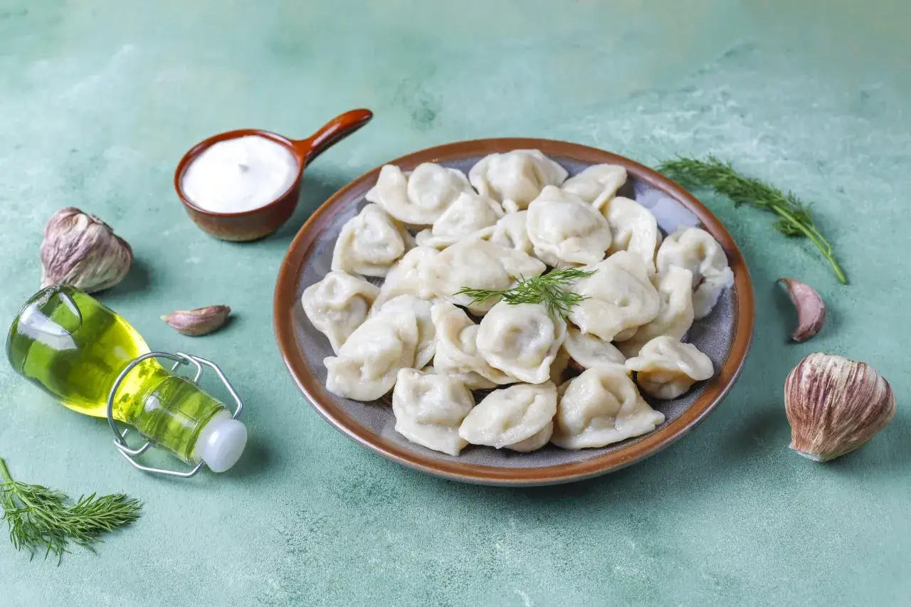 Pyszne pierogi na talerzu, obok śmietana, czosnek i oliwa. Idealne z czym tylko chcesz!