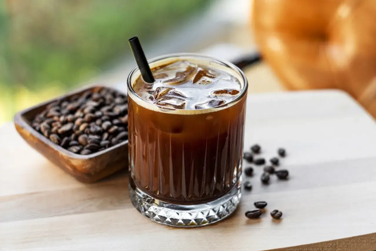 Orzeźwiający cold brew z lodem, obok miseczka z ziarnami kawy. Idealny na gorący dzień.