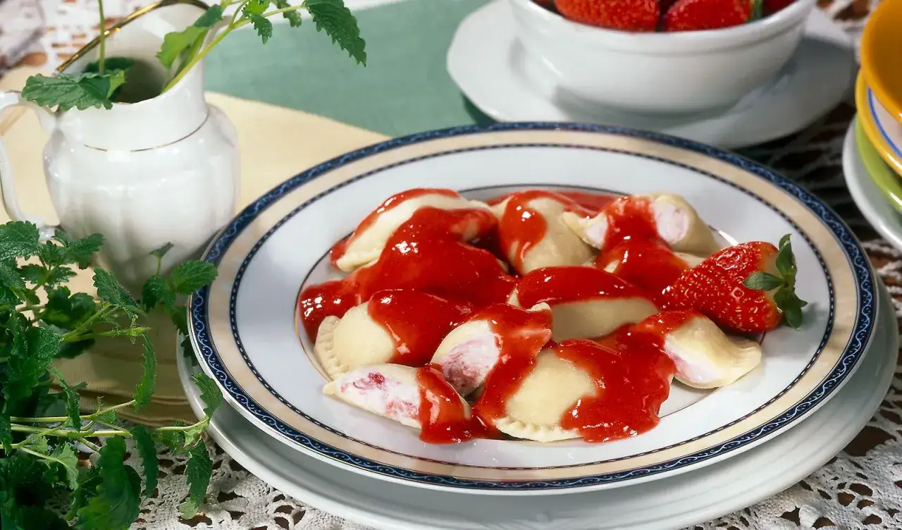 Pyszne pierogi na słodko z truskawkami i sosem. Idealne na deser, udekorowane świeżymi owocami i miętą.