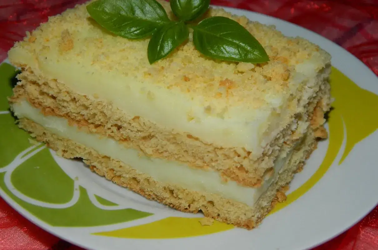 Pyszne ciasto z budyniem, przełożone biszkoptem i posypane kruszonką. Udekorowane listkami bazylii.