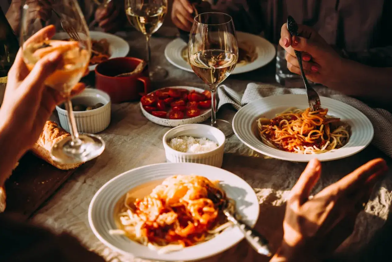 Rodzina delektuje się pyszną kuchnią włoską przy stole, jedząc spaghetti i popijając białe wino.