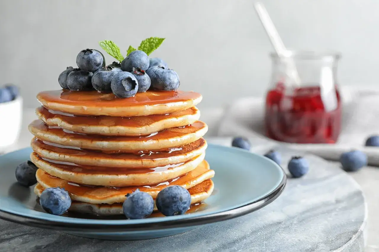 Stos puszystych naleśnik&oacute;w polanych syropem, ozdobiony jagodami i miętą. Idealny przepis na pancake na pyszne śniadanie.