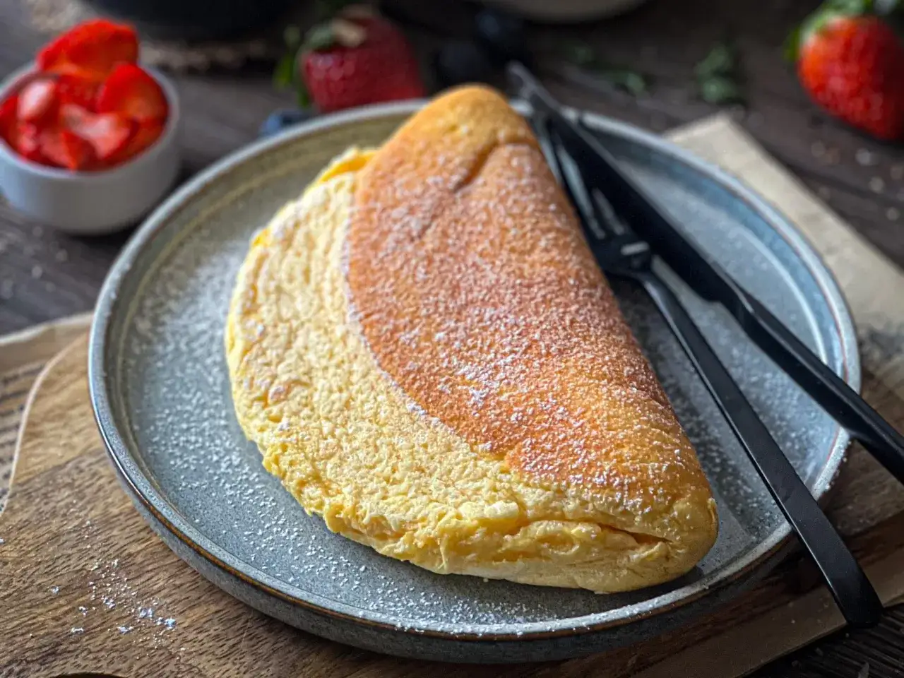 Puszysty omlet na talerzu, posypany cukrem pudrem. Idealny omlet przepis na pyszne śniadanie.