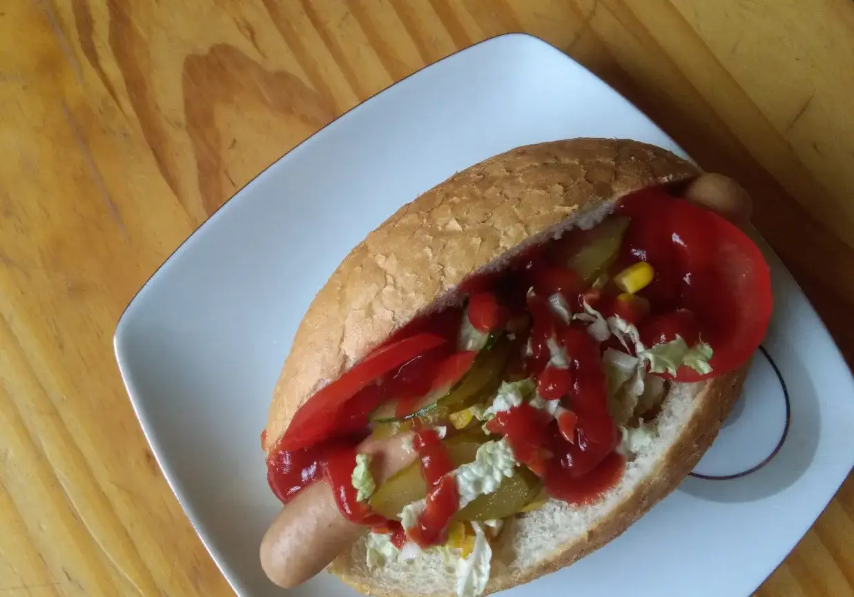 Pyszny hot dog przepis: bułka, parówka, ogórek kiszony, sałata, kukurydza, papryka i ketchup.