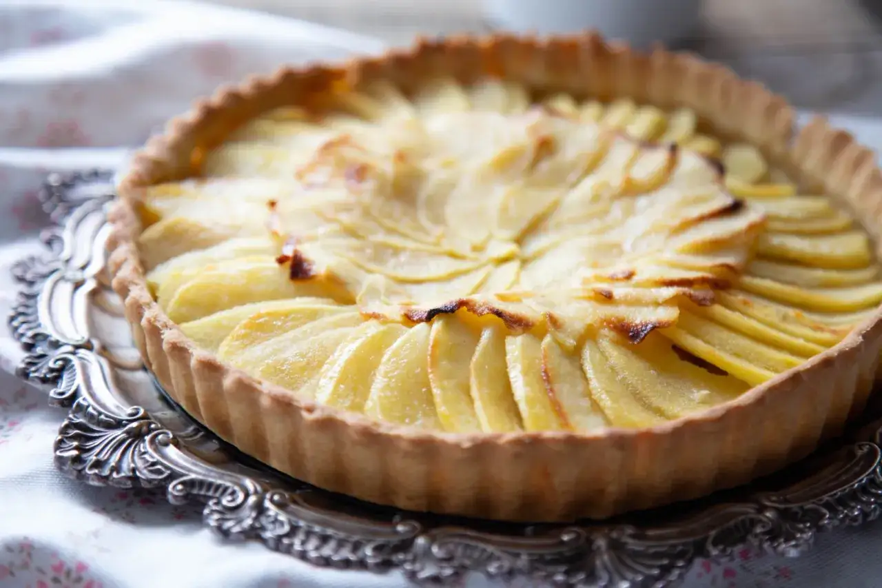 Apetyczna tarta z jabłkami, ułożonymi w fantazyjny wzór, na ozdobnej paterze. Idealna na deser.