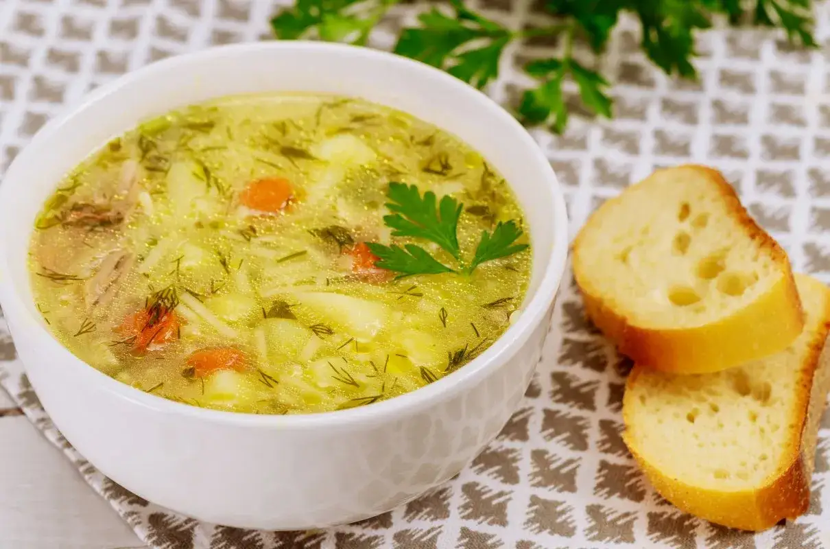 Aromaticzna zupa wiosenna z kawałkami kurczaka, ziemniaków i marchewki, posypana świeżym koperkiem. Obok kromki chleba.