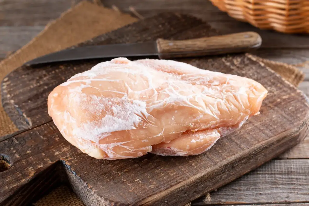 Zamrożony filet z kurczaka na desce, gotowy do szybkiego rozmrożenia. Obok nóż i koszyk.