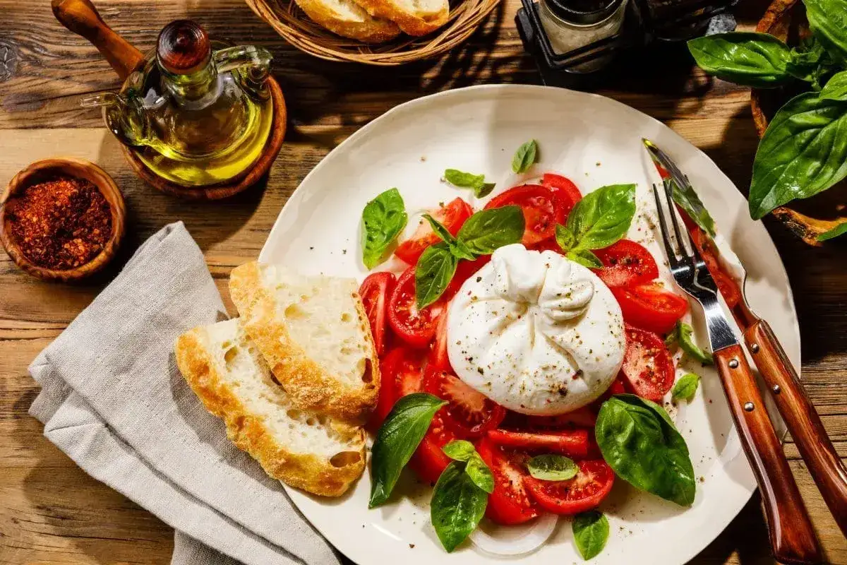 Pyszna burrata z pomidorami i bazylią, podana z chrupiącym pieczywem. To jest właśnie burrata – ser, który rozpływa się w ustach.