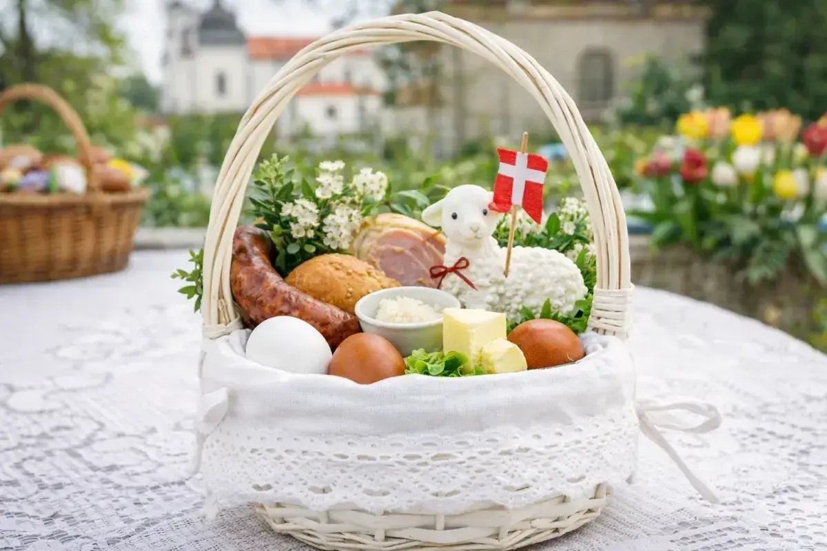 Biały koszyk z tradycyjnymi produktami co do swieconki: jajka, kiełbasa, chleb, masło, baranek z flagą Danii.