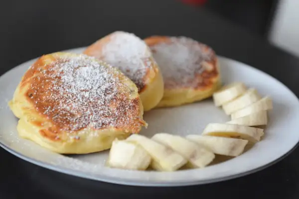 Puszyste, szybkie placuszki na śniadanie posypane cukrem pudrem, obok plasterki banana. Idealne na dobry początek dnia.