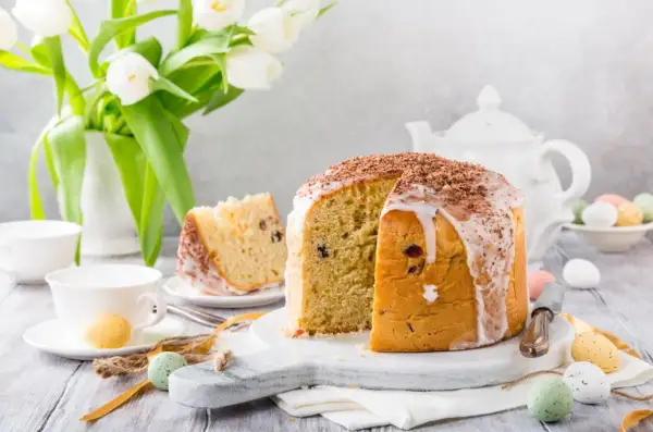 Pyszna babka panettone z lukrem i czekoladą, ozdobiona wielkanocnymi pisankami i białymi tulipanami.