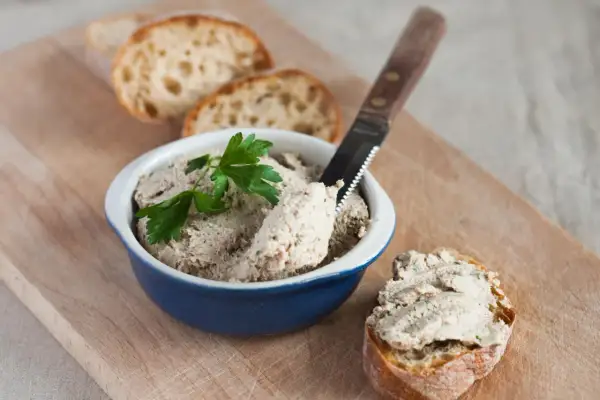 Pyszna pasta z gotowanego kurczaka na chrupiącym pieczywie, udekorowana natką pietruszki. Idealna na przekąskę.