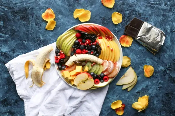 Kolorowa taca z owocami: jabłka, gruszki, kiwi, mango, maliny, borówki, jeżyny i granat. Idealny sposób, jak podać owoce na imprezie.