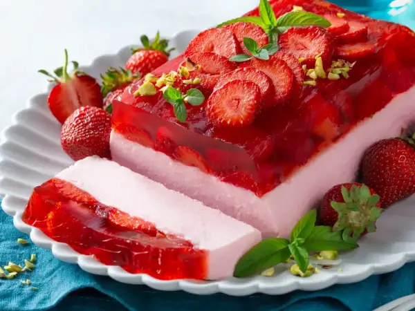 Pyszny deser z truskawkami i galaretką, ozdobiony listkami mięty i pistacjami. Idealny na letnie popołudnie.