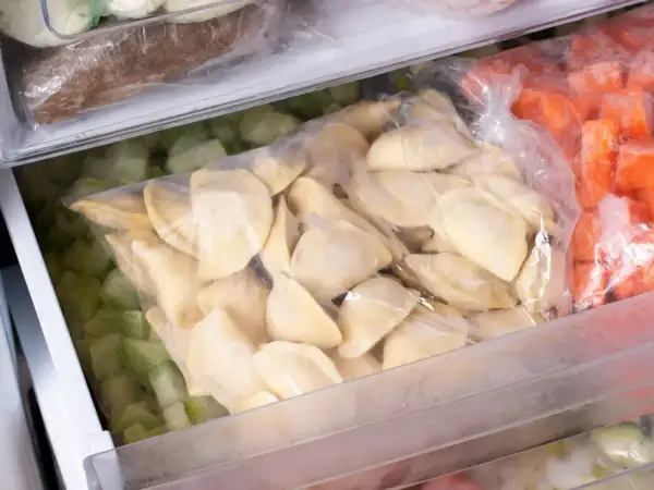 W zamrażarce leżą torby z mrożonkami: pierogi, zielone warzywa i marchewka.