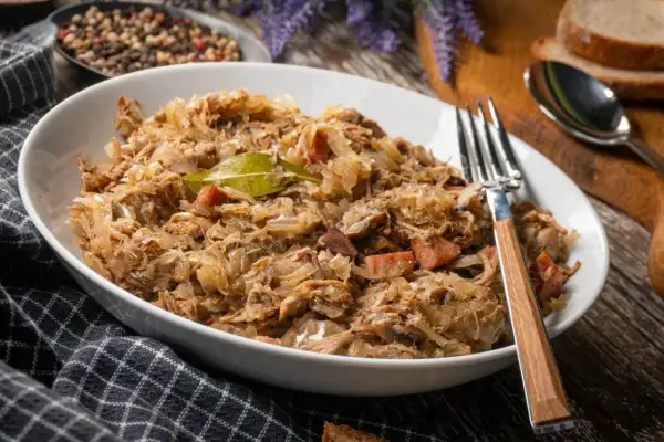 Pyszny bigos w białej misce, z widelcem. Zastanawiasz się, ile może stać bigos w lodówce? Nawet kilka dni, a smakuje coraz lepiej!