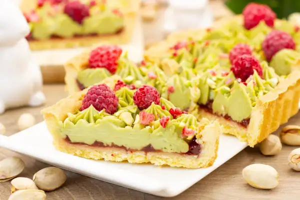 Pyszny mazurek pistacjowy z malinami i chrupiącymi pistacjami, udekorowany zielonym kremem.