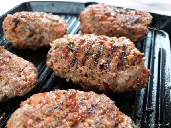 Kebab Adana grillowany na patelni grillowej, z widocznymi kawałkami pomidorów i ziół.
