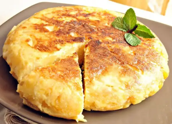 Pyszna tortilla de patatas, złocista i puszysta, z gałązką mięty na wierzchu.