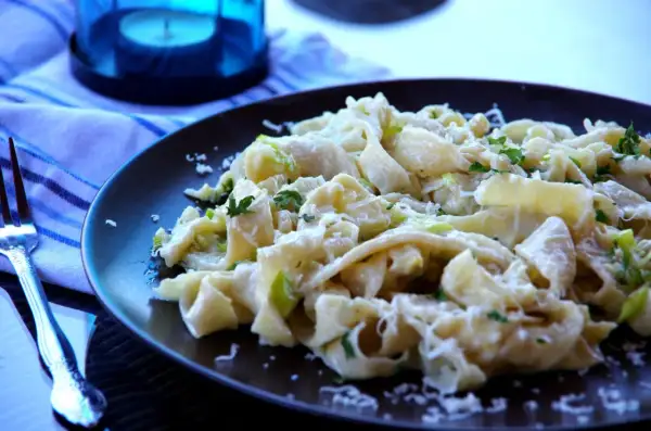 Pyszny makaron z porem, posypany parmezanem i świeżą natką pietruszki, czeka na widelcu.