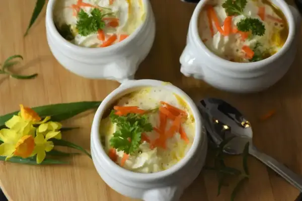 Aksamitna zupa dla dzieci, udekorowana startą marchewką i natką pietruszki. Podana w uroczych białych miseczkach, zachęca do jedzenia.