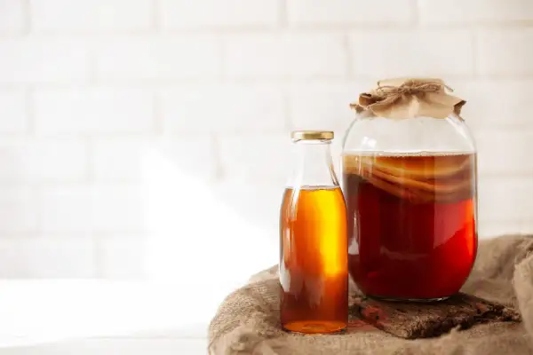 Słoik z ciemnym napojem i widocznym SCOBY, obok butelka z bursztynowym płynem. To jest co to jest kombucha, fermentowany napój.