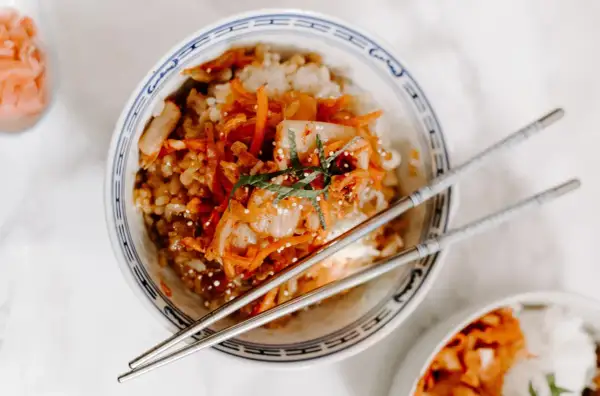 Miseczka ryżu z pikantnym kimchi i marchewką, pałeczki gotowe do jedzenia. Kimchi co to? To fermentowana kapusta.