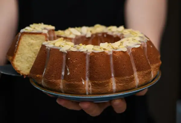 Wilgotna babka wielkanocna, ozdobiona lukrem i płatkami migdałów, prezentuje się apetycznie. Kawałek ciasta został już odcięty.